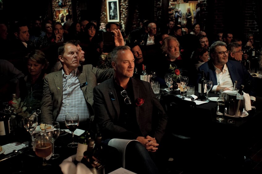 A formal event with attendees seated at tables, glasses of wine, and a dark ambiance. 3