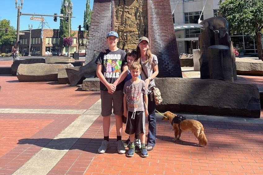 Una familia con un perro en una plaza pública con una escultura y una fuente. 3