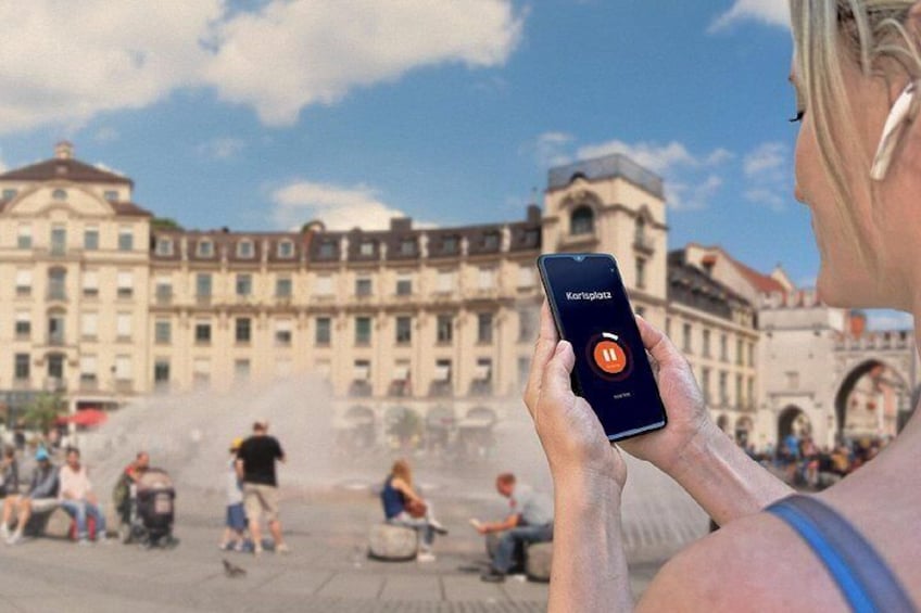 A person using a smartphone with a map application, a historic building, and a fountain in the background. 5