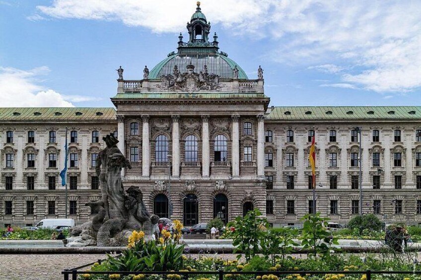A large historic building with a prominent dome and columns, surrounded by a well-maintained garden and a statue. 3