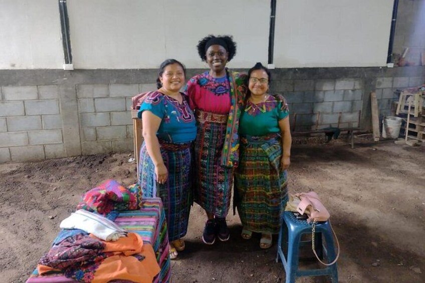 Tres mujeres con atuendo tradicional de pie en un entorno exterior con suelo de tierra y un edificio al fondo. 3