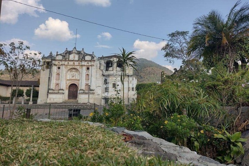 Una iglesia histórica con un campanario, rodeada de vegetación tropical y montañas al fondo. 1