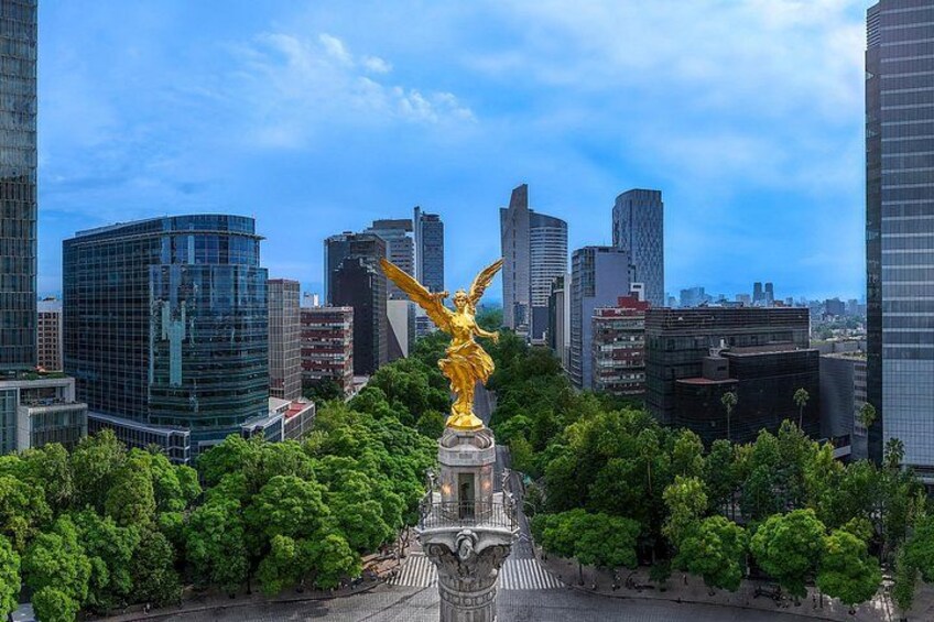 A golden statue in a park with a city skyline in the background. 4