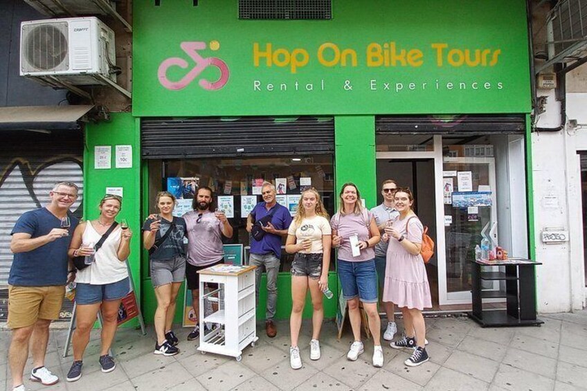 Een groep mensen voor een groene winkel met een bord waarop staat 'Hop On Bike Tours Rental & Experiences'. 2