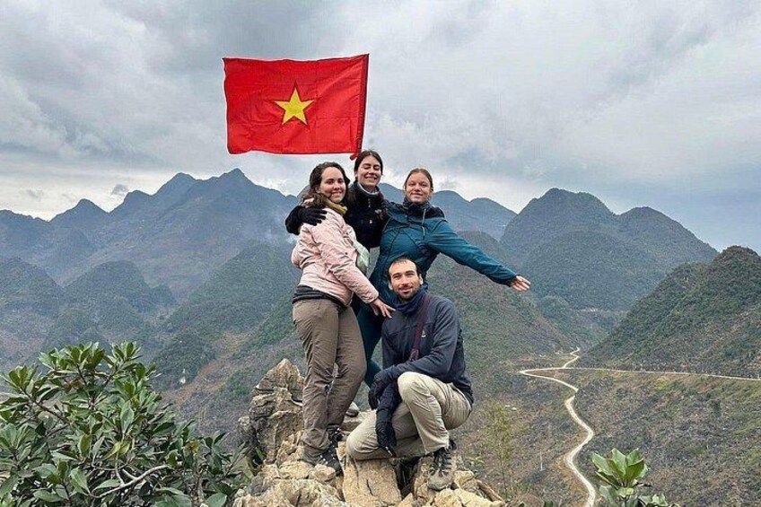 A group of people posing with a flag, a mountainous landscape, and a winding road. 5