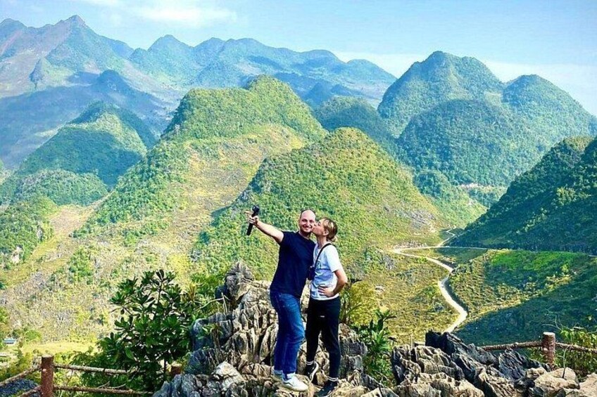 A person taking a selfie with a child on a rocky outcrop overlooking a mountainous landscape. 3