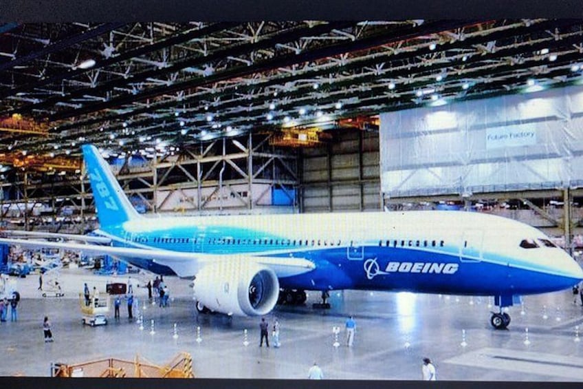A large airplane with the Boeing logo, surrounded by a spacious indoor area with high ceilings and industrial lighting. 5