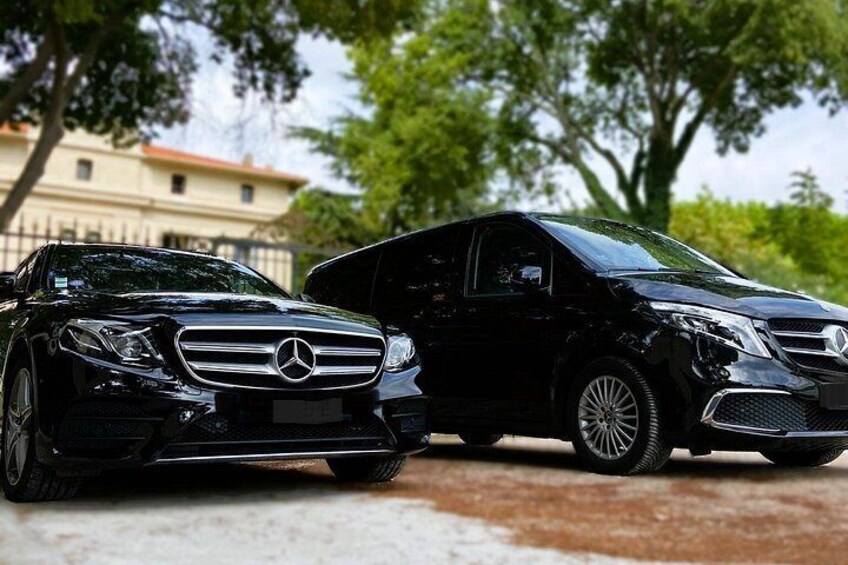 Two black Mercedes-Benz cars parked on a paved surface with trees and a building in the background. 1