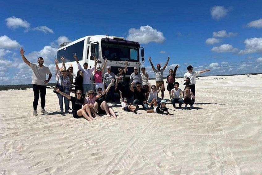 A group of people posing with a bus on a sandy beach under a clear sky. 5