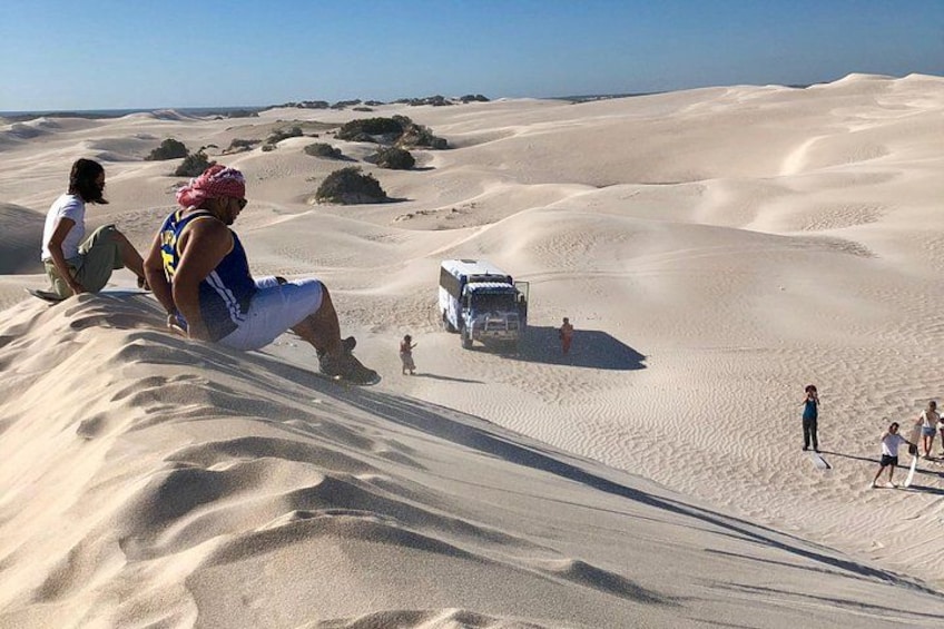 A desert landscape with sand dunes, a person sitting on a dune, and a vehicle in the background. 3