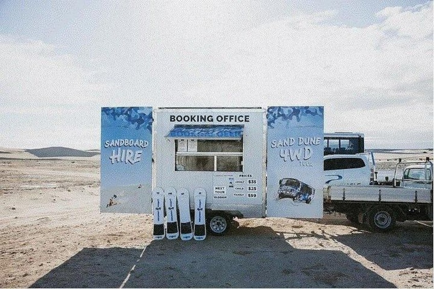 Une remorque servant de bureau d’accueil, avec une enseigne indiquant « Location de sandboards » et « Excursion en 4x4 dans les dunes de sable ». 2
