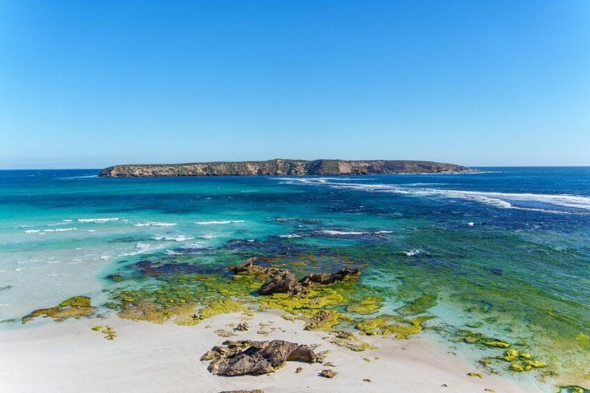A coastal landscape with clear turquoise waters, a sandy beach, and rocky outcrops. 1