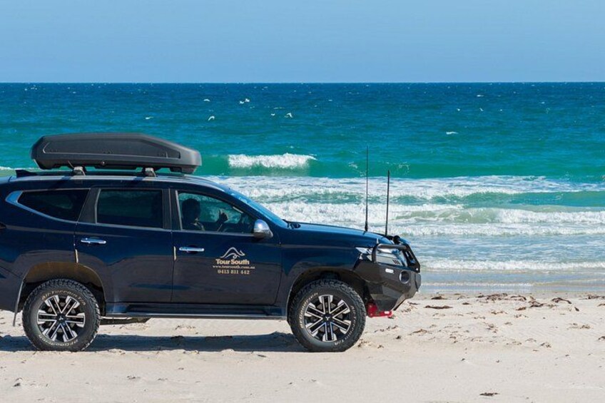 A dark blue SUV parked on a sandy beach with the ocean in the background. 5