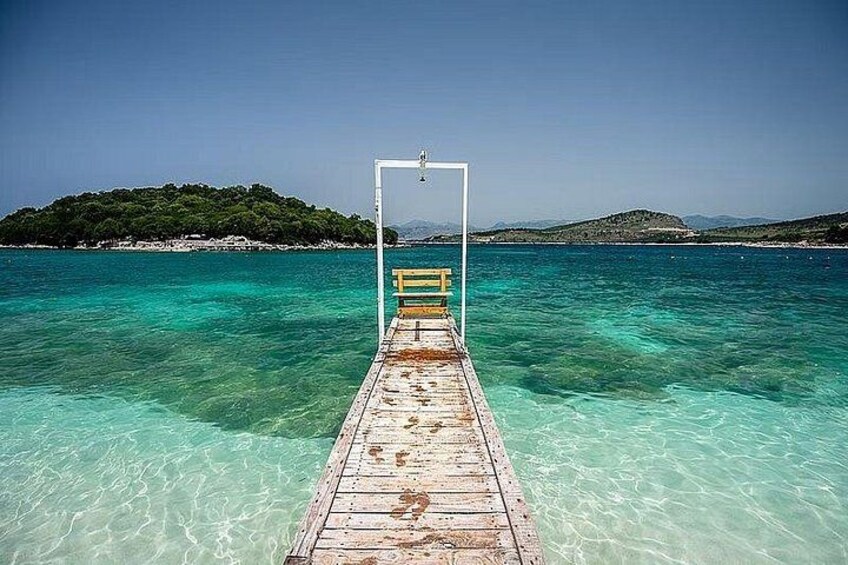 Un muelle de madera se adentra en un mar turquesa cristalino, con una pequeña isla al fondo. 3