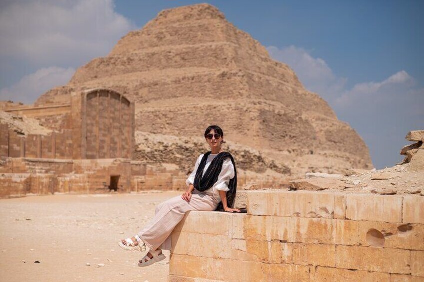 Eine Person sitzt auf alten Steinblöcken, im Hintergrund eine Pyramide. 2