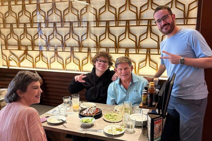 Un grupo de personas cenando en un restaurante con una pared decorada al fondo. 1
