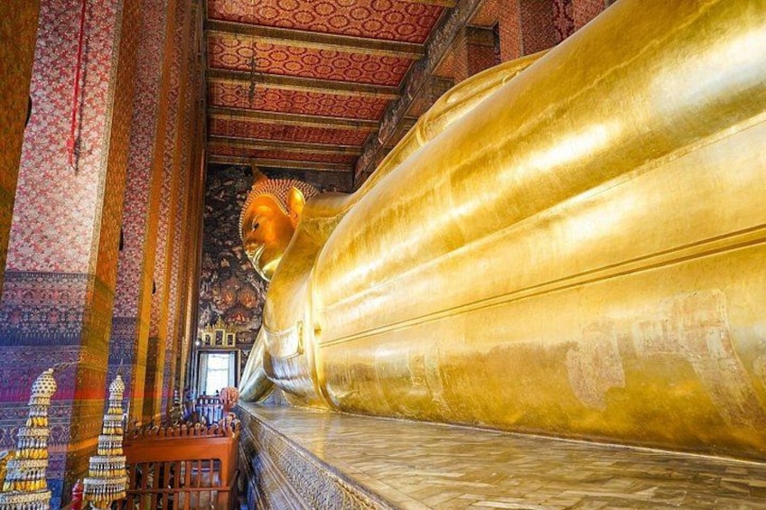 A large golden Buddha statue in a temple with intricate wall patterns and a tiled floor. 2