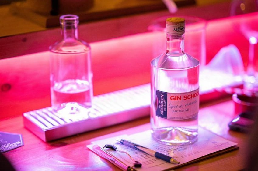 A bottle of gin, a keyboard, and some papers on a table. 2
