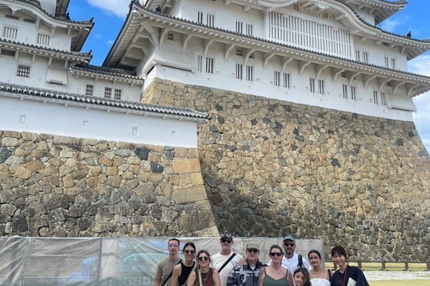 A group of people in front of a large castle with a stone wall and traditional architecture. 4