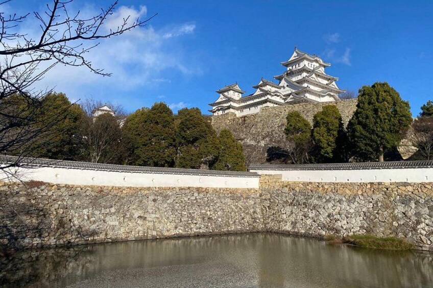 A traditional Japanese castle with multiple tiers, a stone wall, and a calm pond in the foreground. 3