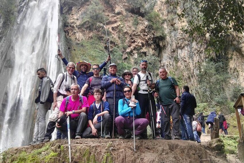 Un groupe de personnes se tient sur un promontoire rocheux, avec une cascade en arrière-plan. 2