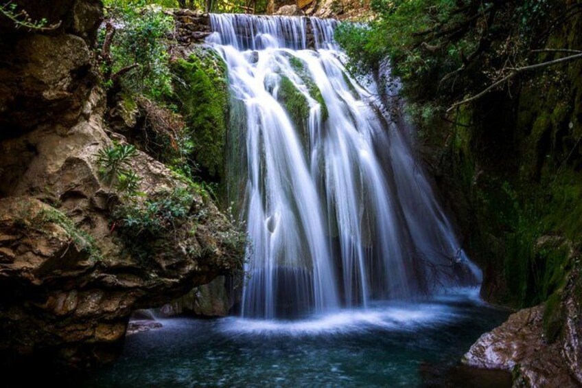 Ein Wasserfall stürzt über Felsen in einen Pool, umgeben von üppigem Grün. 2