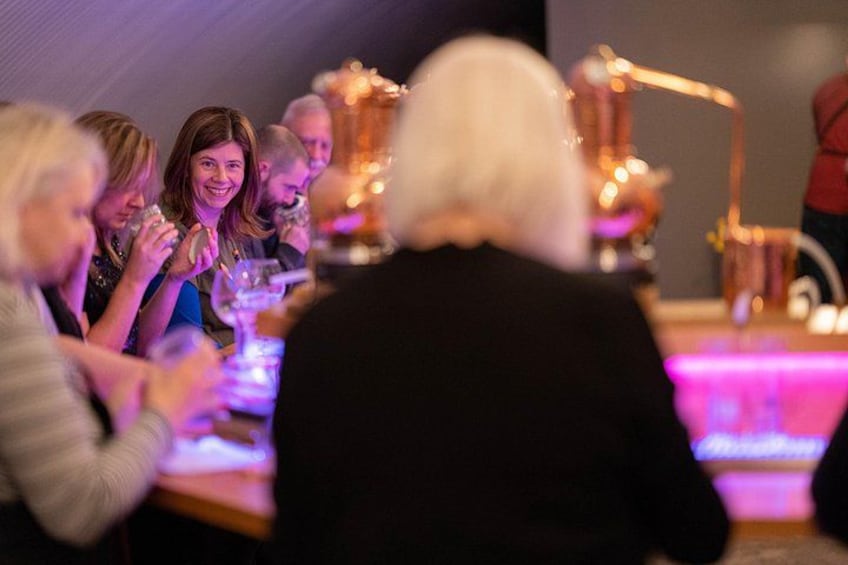 Eine Gruppe von Personen sitzt an einem Tisch, im Hintergrund ist eine beleuchtete Bar zu sehen. 5