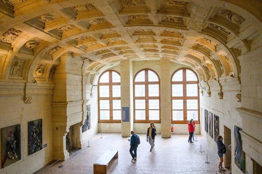 Un interior con ventanas arqueadas, un techo alto con detalles tallados y algunos visitantes. 4