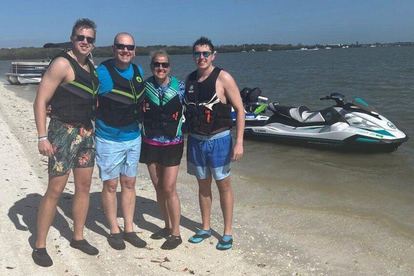 Quattro persone in piedi su una spiaggia sabbiosa, con un jet ski sullo sfondo. 3