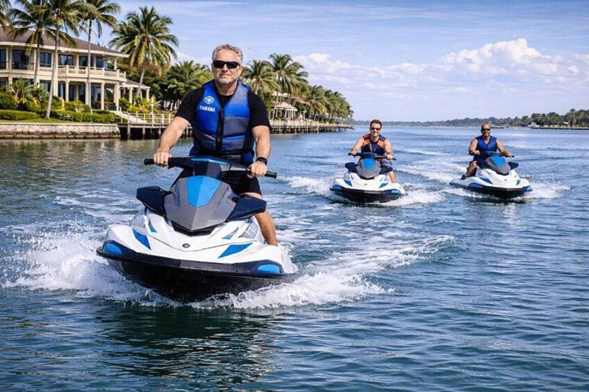 Tre persone che guidano jet ski su un'acqua calma, con palme e un edificio sullo sfondo. 4