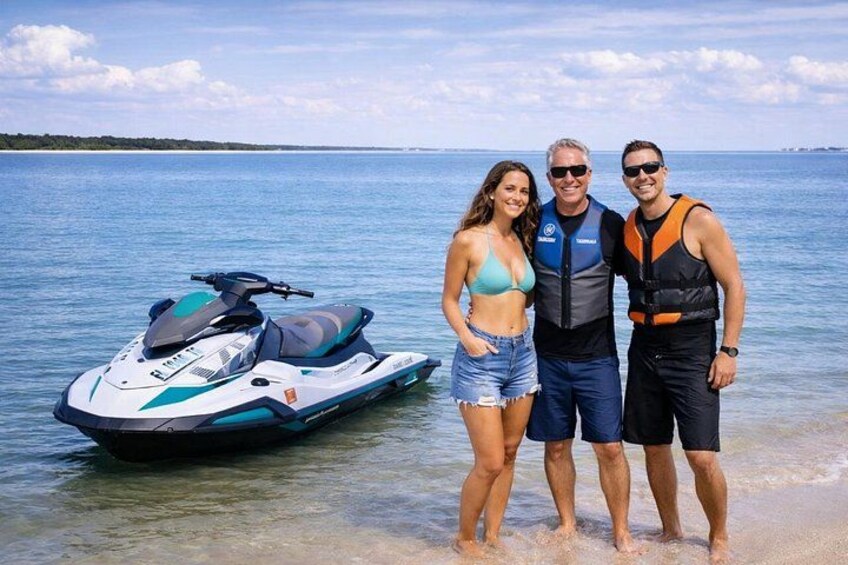 Un jet ski, una persona con salvagente blu e un'altra con salvagente arancione in piedi su una spiaggia. 2