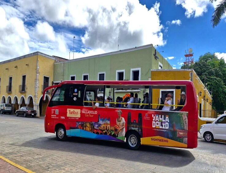 A red double-decker bus with tourists on board, parked in front of a building with arches. 3