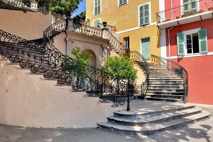 Un conjunto de escalones de piedra con barandillas de hierro ornamentales que conducen a un edificio con fachada roja y contraventanas verdes. 2