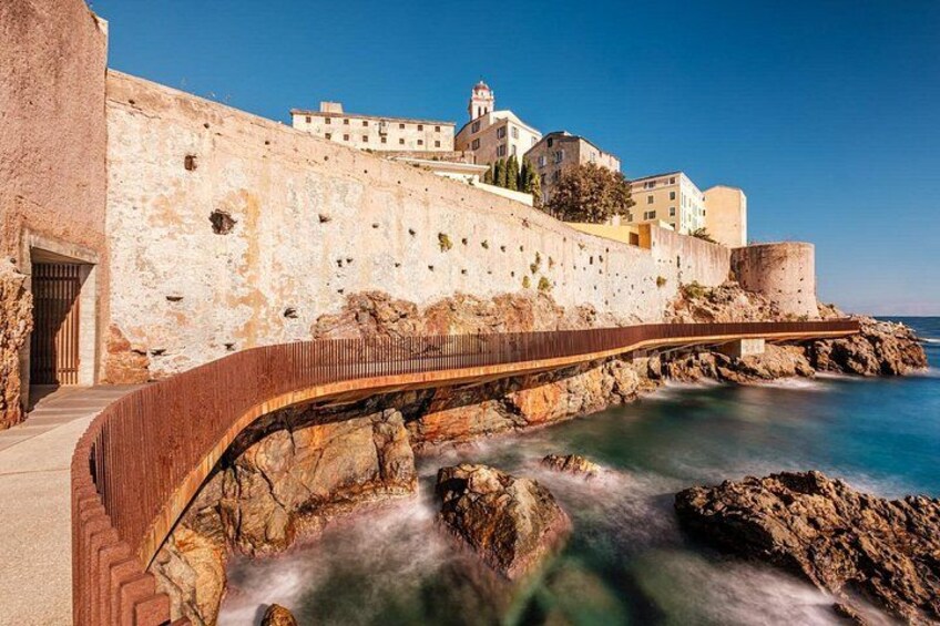 Una fortificación costera con un puente, costa rocosa y edificios al fondo. 4