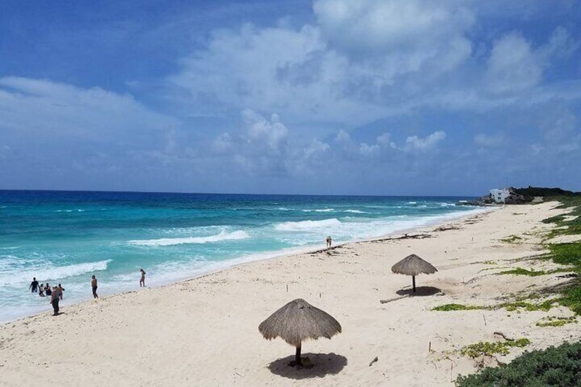 Une plage à l’eau turquoise et limpide, quelques personnes qui se promènent, et deux parasols en chaume. 3