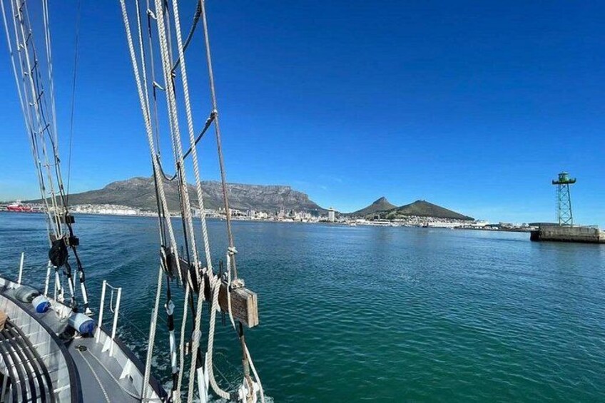 Een zeilboot met masten en lijnen, kalm water, een vuurtoren en een bergachtige kustlijn. 3