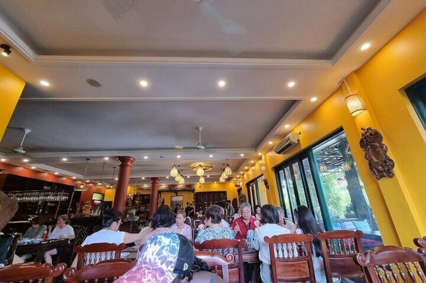 Interior de restaurante con paredes amarillas, sillas de madera y personas cenando. 1