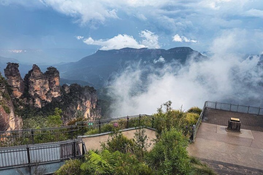 A mountainous landscape with rock formations, a railing, and a cloudy sky. 1