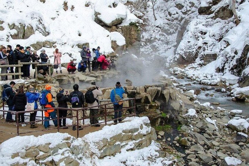 A group of people observing a hot spring in a snowy mountainous area. 3