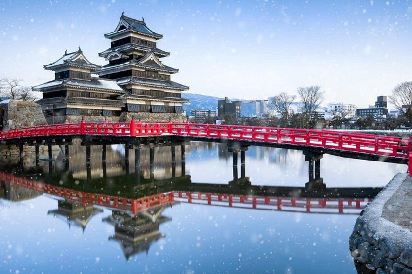 A traditional Japanese castle with multiple tiers, a red bridge, and a calm body of water reflecting the structures. 5