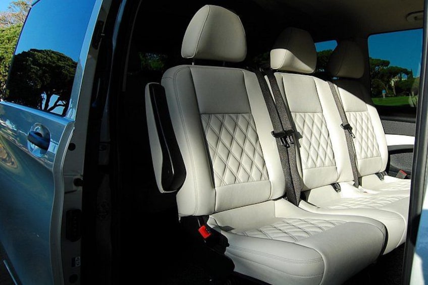 A vehicle's interior with two front seats, seat belts, and a rearview mirror. 2