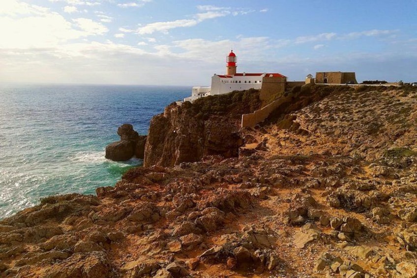 Un paisaje costero con terreno rocoso, un faro y un edificio blanco. 3