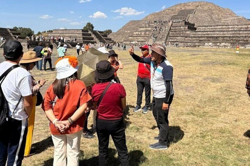A group of tourists at a historical site with a large pyramid in the background. 1