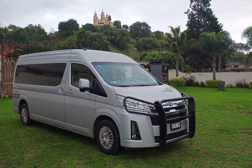 A silver minivan parked on a grassy area with a backdrop of trees and a distant building. 4