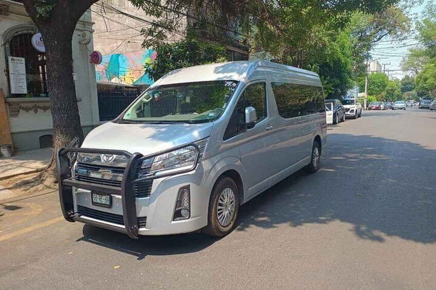 A silver van parked on a street with trees and buildings in the background. 2