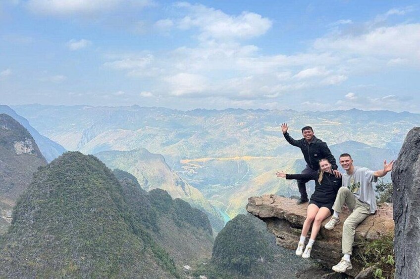 Three people on a rocky outcrop with a mountainous landscape in the background. 4