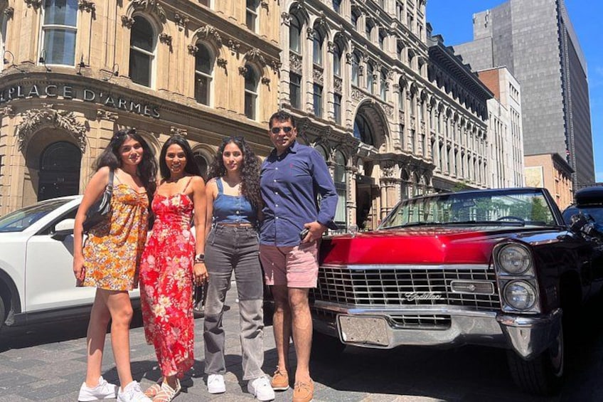 A group of people posing in front of a vintage car and a historic building with ornate architecture. 5