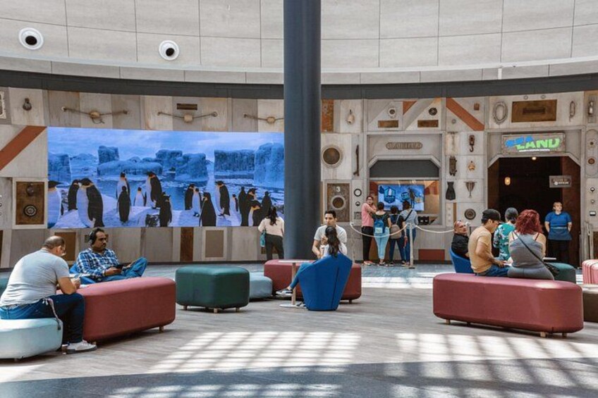 A lobby with seating areas, a large digital screen displaying penguins, and a sign that reads 'LAND'. 2