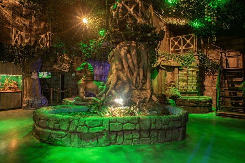 A large tree with a stone base, surrounded by greenery and a dimly lit environment. 4