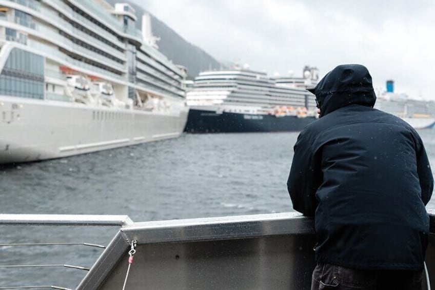 A person on a boat looking at a large cruise ship in the distance. 1